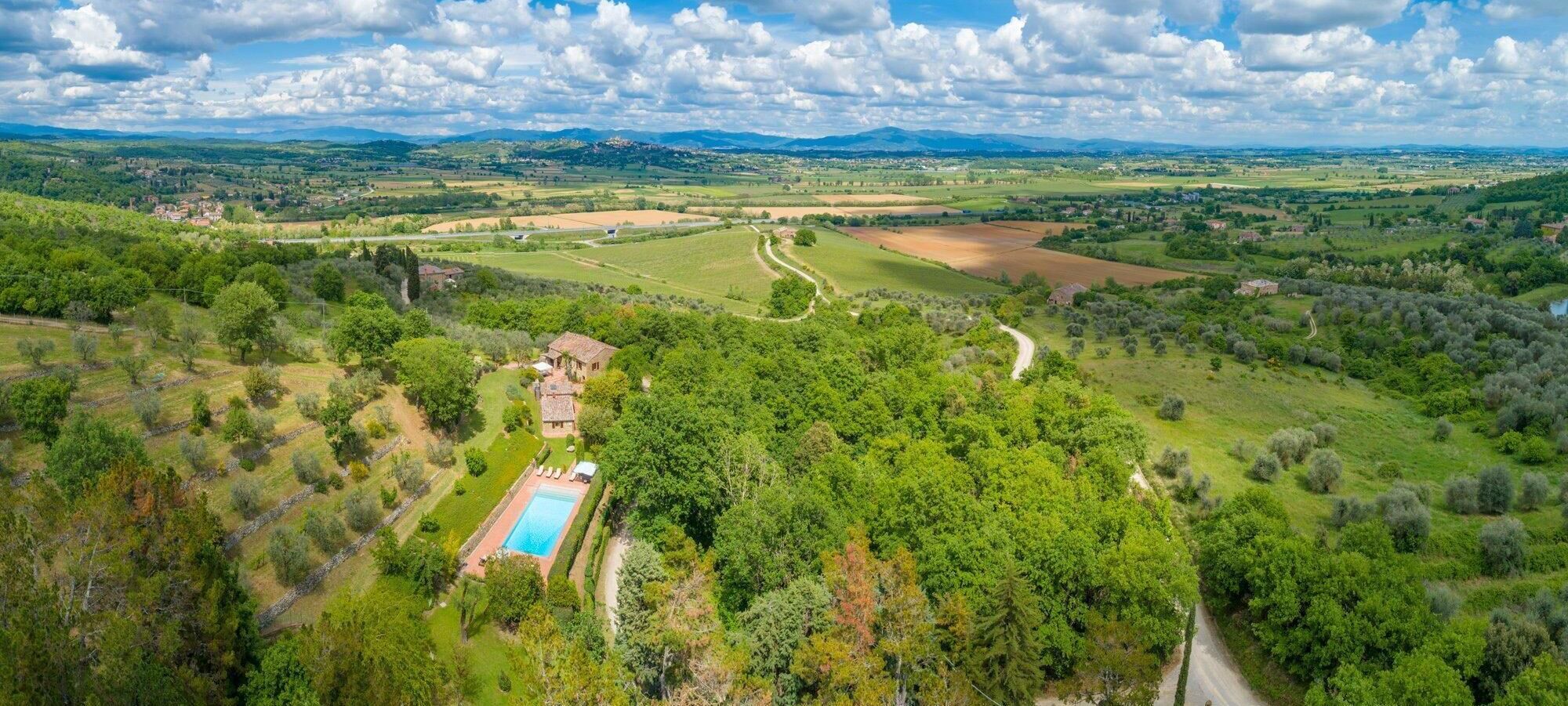 Vista aerea di una proprietà in campagna con piscina, strada sinuosa e campi circostanti.