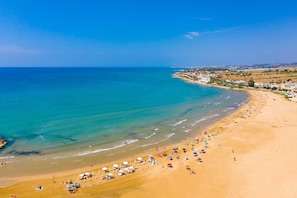 Une plage aux eaux d’un bleu limpide, avec un rivage sablonneux et une rangée de parasols.