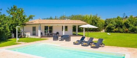 Una casa con piscina, mobiliario de exterior y un patio cubierto.
