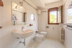 A bathroom with a sink, toilet, bidet, and a window.