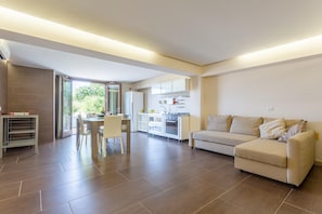 A modern living room with a sofa, a dining table with chairs, and a kitchen area with cabinets and appliances.
