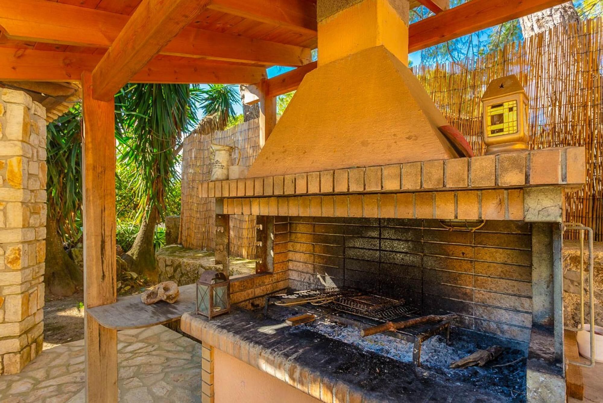 Un horno de ladrillo al aire libre con chimenea, rodeado de muros de piedra y una pérgola de madera.