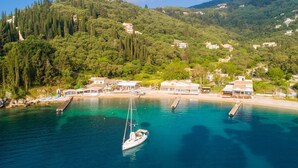 A coastal area with a clear blue sea, a sailboat docked, and buildings on a hillside. - Villa Durrell Large Private Pool Walk to Beach A C Wifi - 2927 (Corfu)