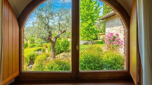Una habitación con un amplio ventanal arqueado que da a un jardín con diversos árboles y arbustos.
