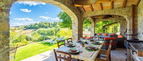An outdoor dining area with stone arches, a view of the countryside, and a wooden ceiling.
