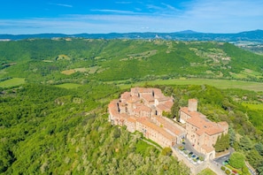 Vista aérea de un complejo de edificios históricos de piedra, rodeado de colinas y campos verdes exuberantes.