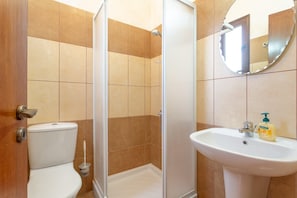 Un baño con inodoro, ducha e lavabo con espejo.