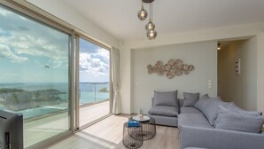 A modern living room with a grey sofa, a round coffee table, and a large window offering a view of the sea. - Villa Lassi Illios Large Private Pool Walk to Beach Sea Views A C Wifi - 3055 (Kefalonia)