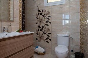 Ein Badezimmer mit weißem Waschbecken, Spiegel und Toilette. Eine Wand mit dekorativen Fliesen und einem floralen Muster. Auf dem Boden steht ein Korb mit Handtüchern.