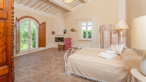 Een slaapkamer met een bed, een stoel, een open haard en een raam met gordijnen.