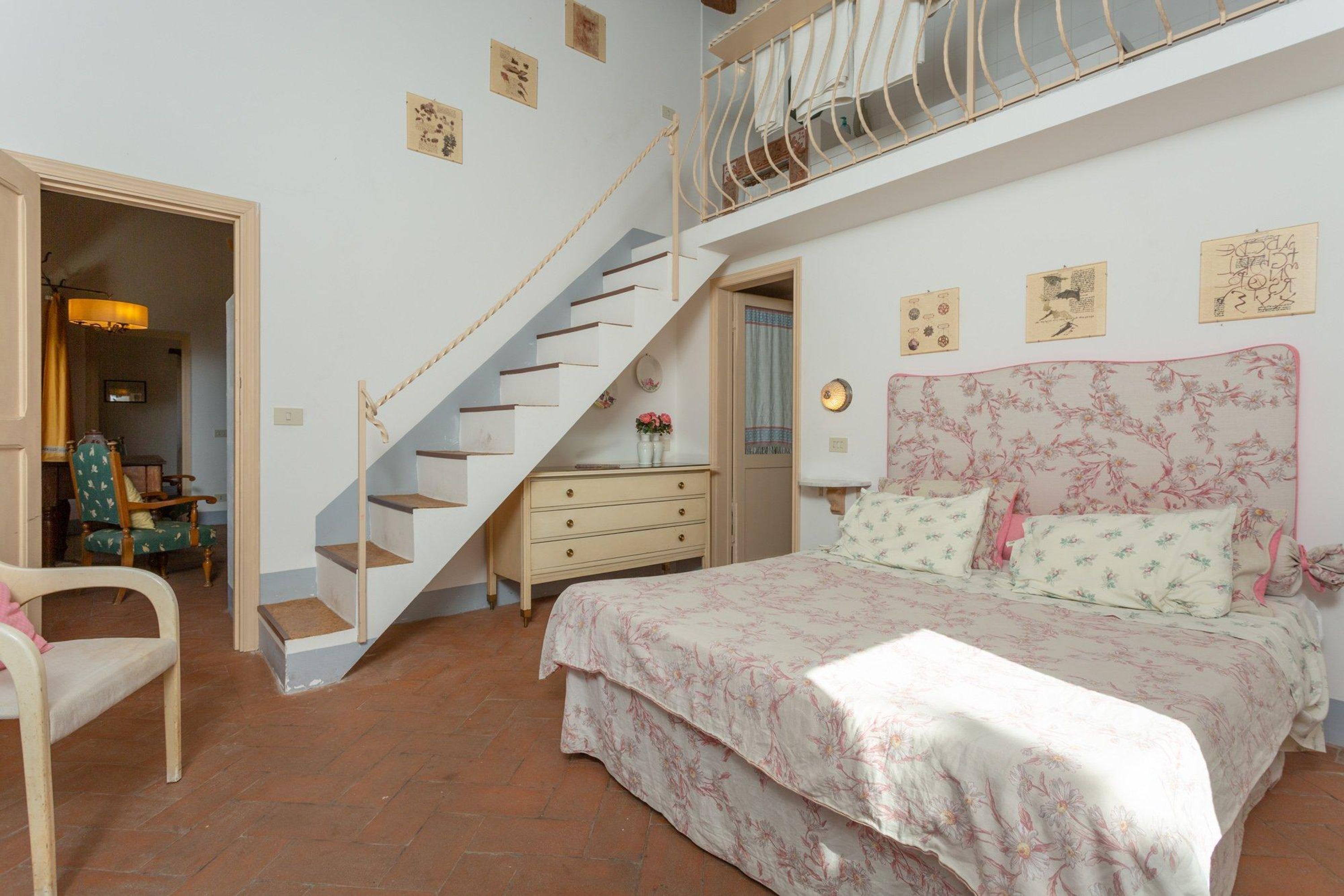 Une chambre à coucher comprenant un lit, une commode, une chaise, un escalier et un balcon.