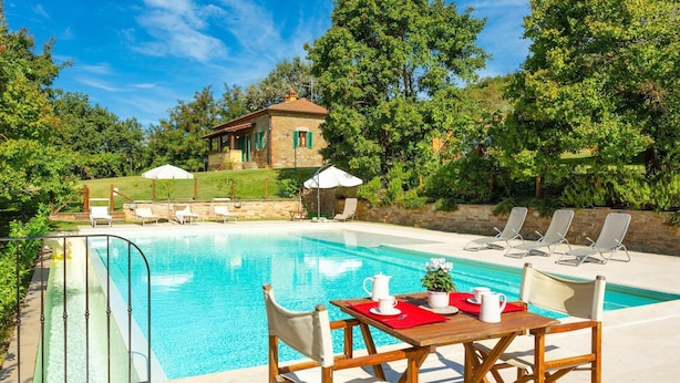 Un espace piscine avec des chaises longues, une table recouverte d’un set de table rouge et un petit bâtiment en arrière-plan.
