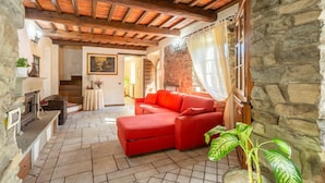 A cozy living room with a red sofa, stone walls, a fireplace, and a wooden ceiling. - Villa Casale Le Selve Large Private Pool Wifi - 3099 (Castiglione di Garfagnana)