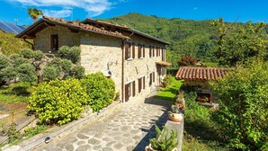 A stone building with a tiled roof, surrounded by lush greenery and a mountain backdrop. - Villa Casale Le Selve Large Private Pool Wifi - 3099 (Castiglione di Garfagnana)