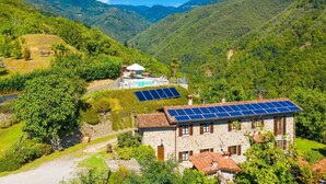 A stone building with a swimming pool and solar panels, surrounded by lush greenery and mountains. - Villa Casale Le Selve Large Private Pool Wifi - 3099 (Castiglione di Garfagnana)