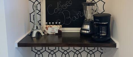 A coffee station with a chalkboard sign, a coffee maker, and a collection of coffee beans.