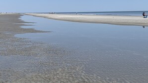 Ein weiter Sandstrand mit ruhigem Wasser und ein paar Personen in der Ferne.