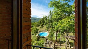 A view of a swimming pool surrounded by a wooden fence and trees, viewed from a window with a brick wall. - Villa Bellavista Large Private Pool Wifi - 3122 (Ortignano Raggiolo)