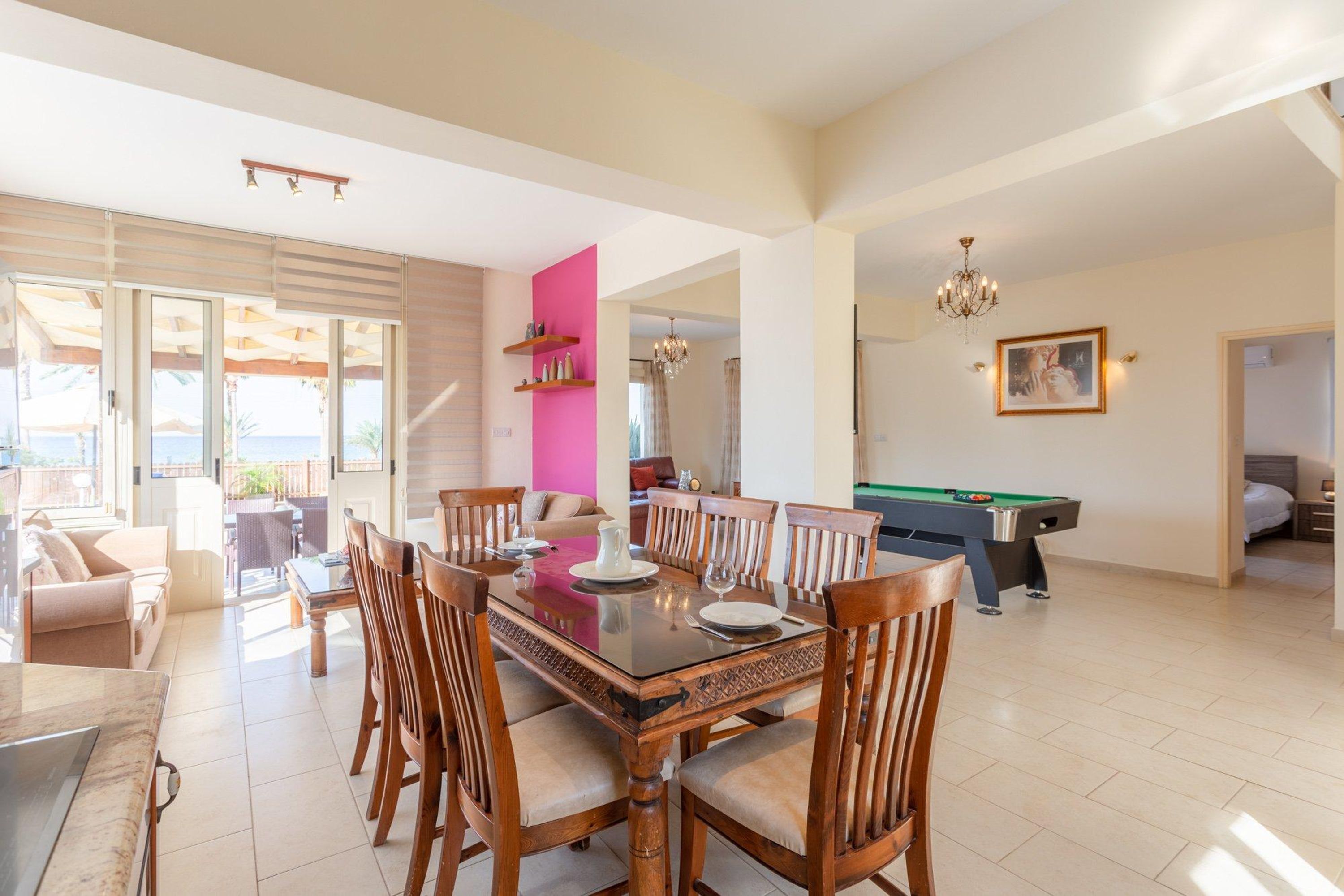 Amplia sala de estar con mesa de comedor, sillas, mesa de billar y un ambiente luminoso gracias a sus grandes ventanales.