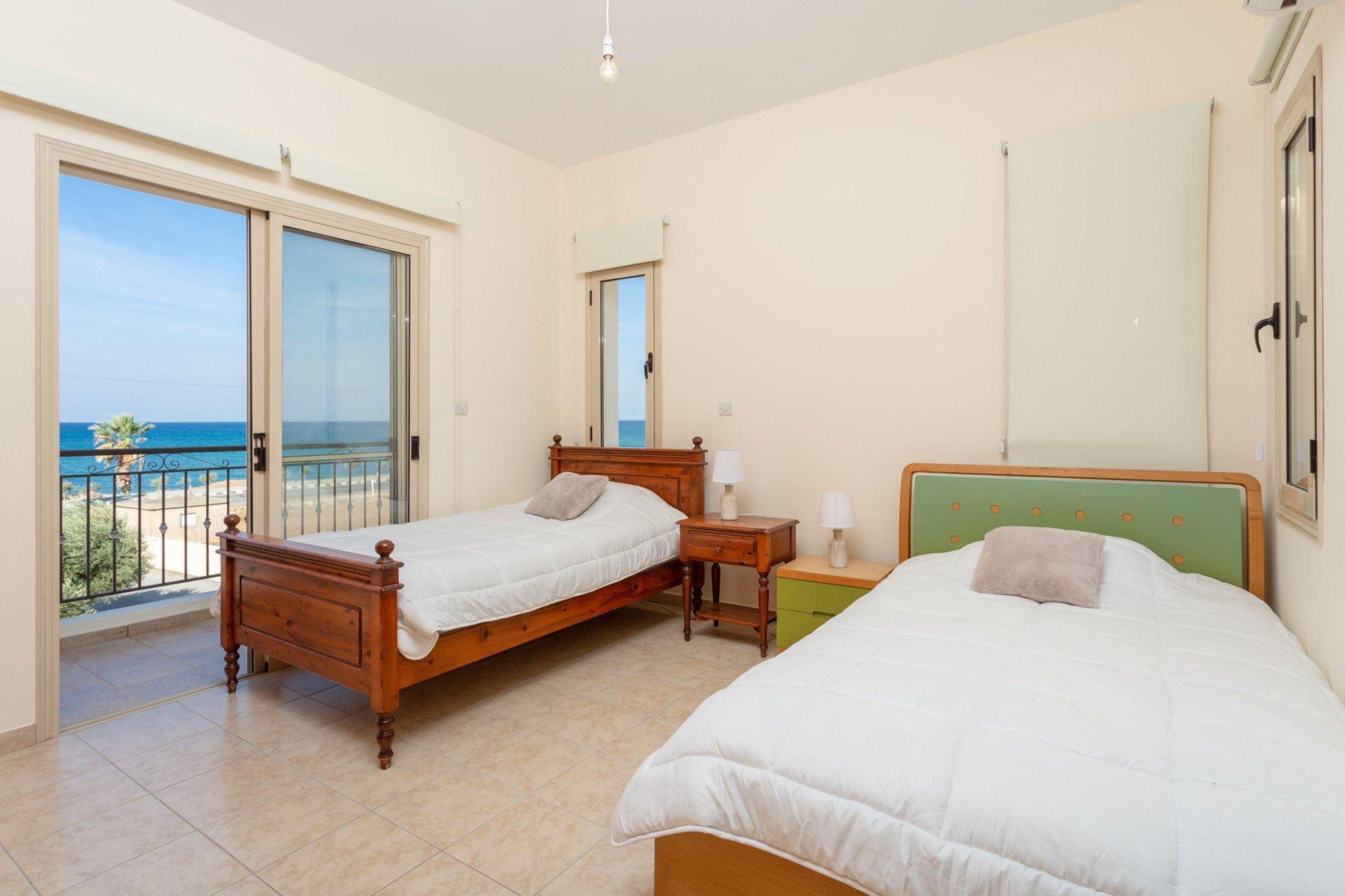 Une chambre à coucher avec deux lits en bois, une tête de lit verte et un balcon avec vue sur la mer.