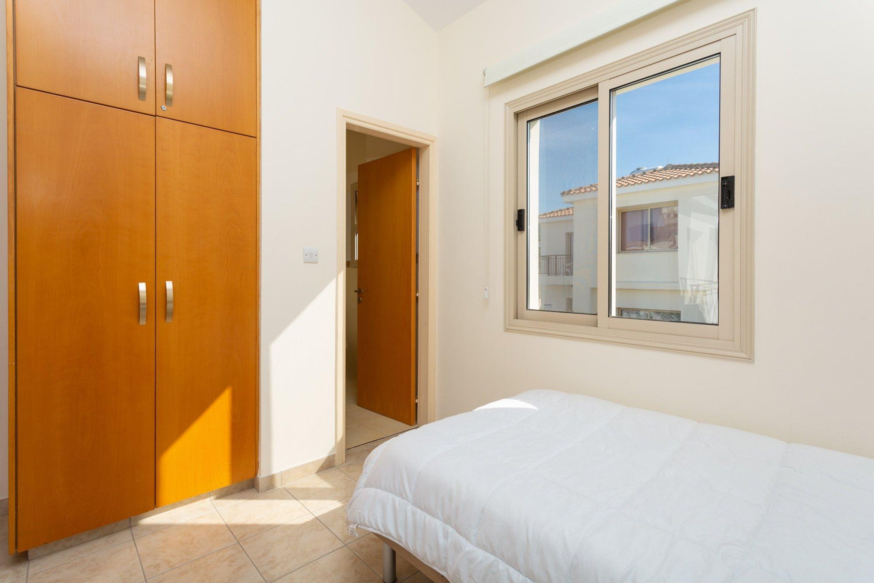 A bedroom with a bed, a wardrobe, and a window with a view of a building.