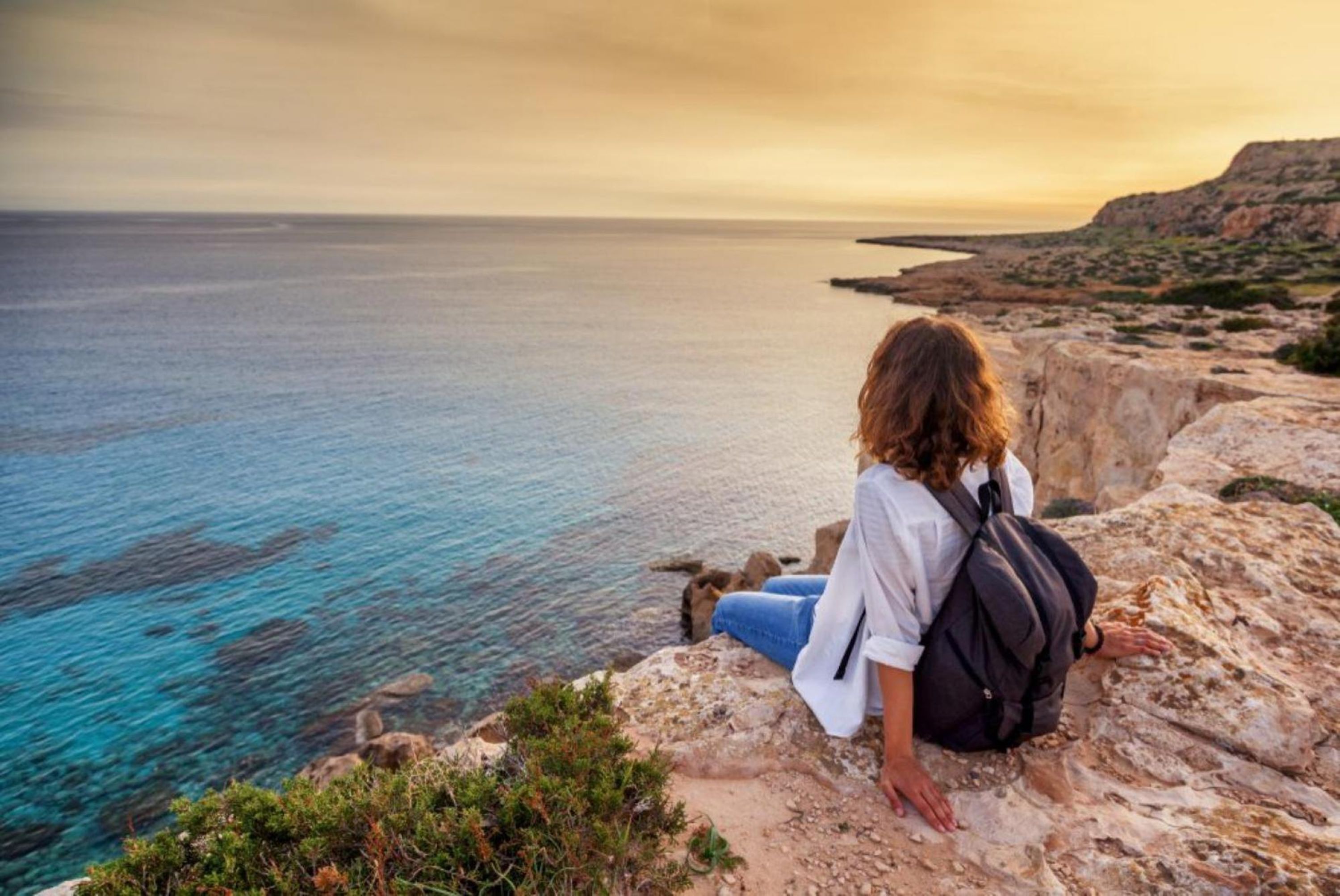 A person sitting on a rocky cliff overlooking a body of water.
