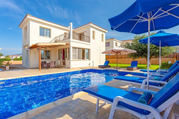 A modern two-story house with a swimming pool, outdoor seating, and umbrellas.