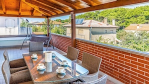 Un espacio de estar al aire libre cubierto con muebles de mimbre y una mesa de vidrio, con vistas a un barrio residencial.