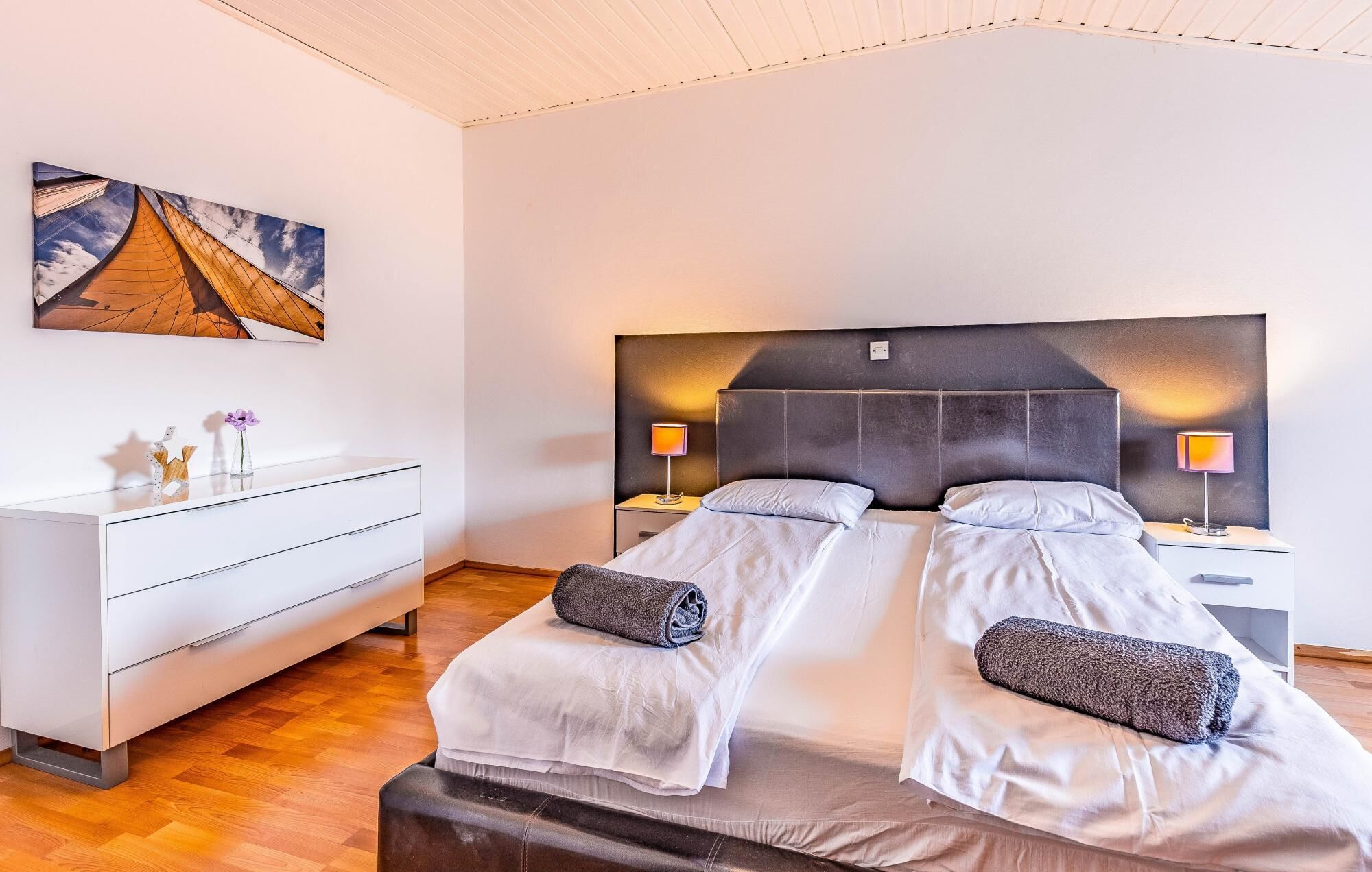 Et moderne hotelværelse med en stor seng, sengeborde med lamper, en hvid kommode og et maleri på væggen.