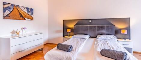 Et moderne hotelværelse med en stor seng, sengeborde med lamper, en hvid kommode og et maleri på væggen.