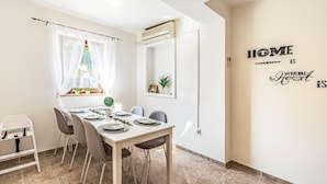 Comedor con mesa blanca dispuesta para cuatro comensales, techo alto y pared con una cita motivacional.