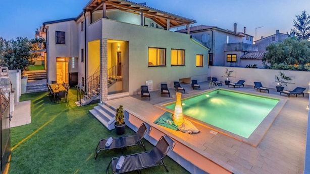 Una casa moderna de dos pisos con piscina, mobiliario exterior y un césped bien cuidado.