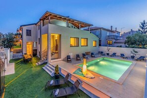 Una casa moderna de dos pisos con piscina, mobiliario exterior y un césped bien cuidado.