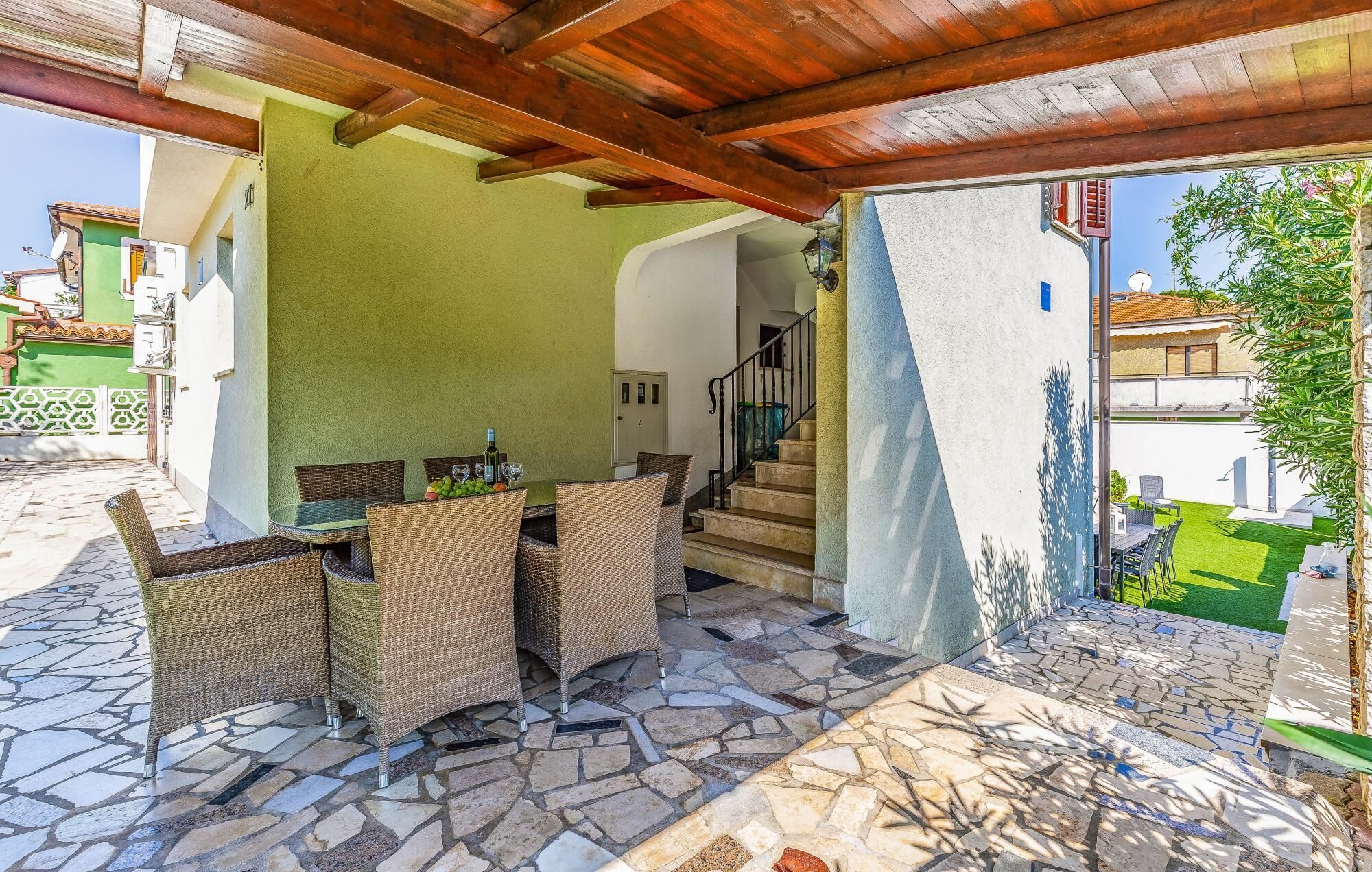 An outdoor patio with wicker furniture, a stone floor, and a view of a green garden.
