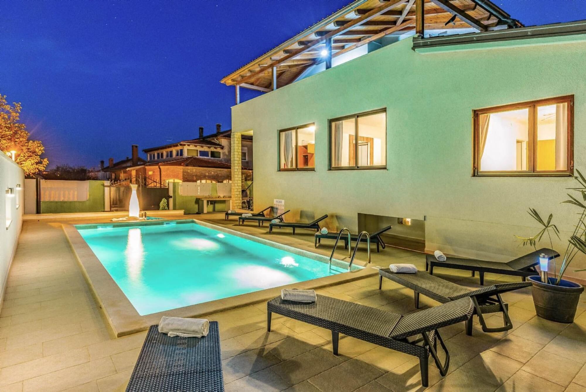 Una piscina con lettini e una vasca idromassaggio, circondata da un edificio con ampie finestre.
