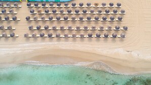 An aerial view of a beach with rows of umbrellas and a clear, shallow water area.