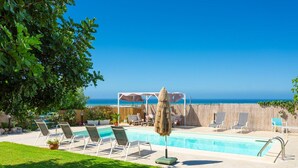 A poolside area with lounge chairs and a view of the ocean.