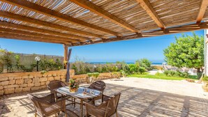 An outdoor patio with wicker furniture and a view of the sea.