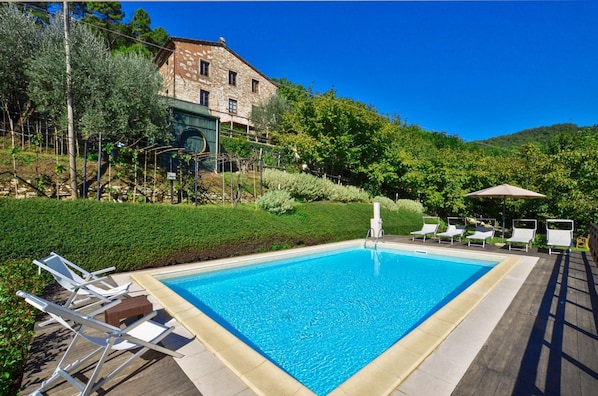 A rectangular swimming pool with clear blue water, surrounded by a wooden deck and white lounge chairs.