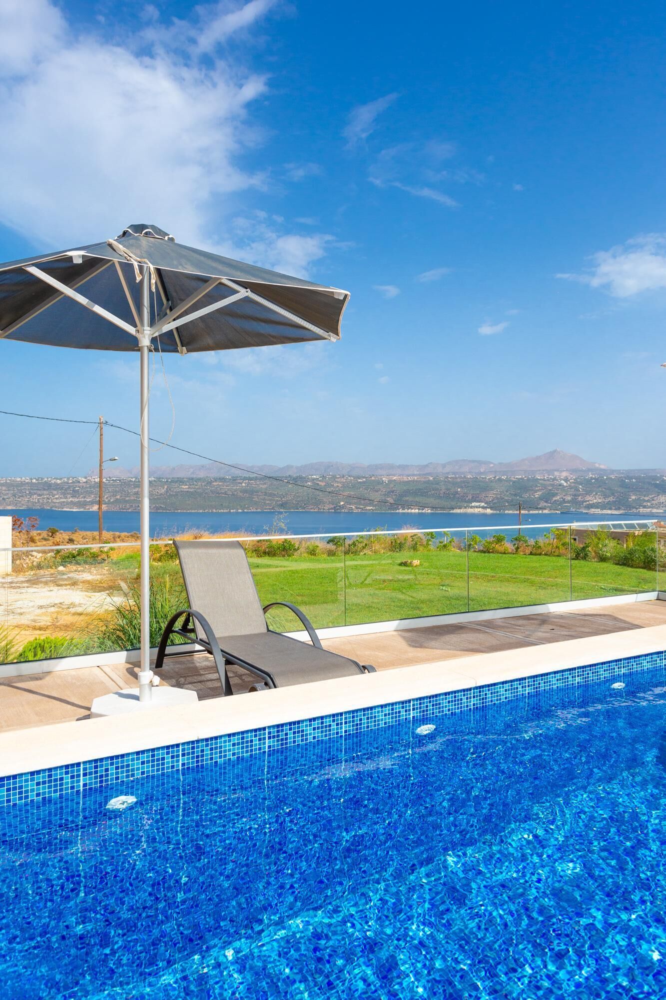 A swimming pool with a clear view of the sea and mountains in the background.