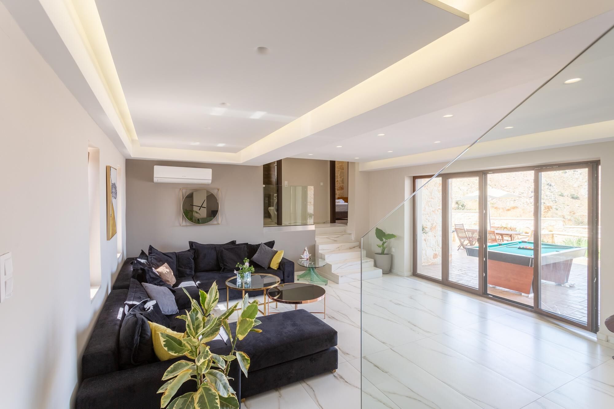 Una sala de estar moderna con un sofá negro, una mesa de centro redonda y un gran ventanal con vistas a una zona de piscina.