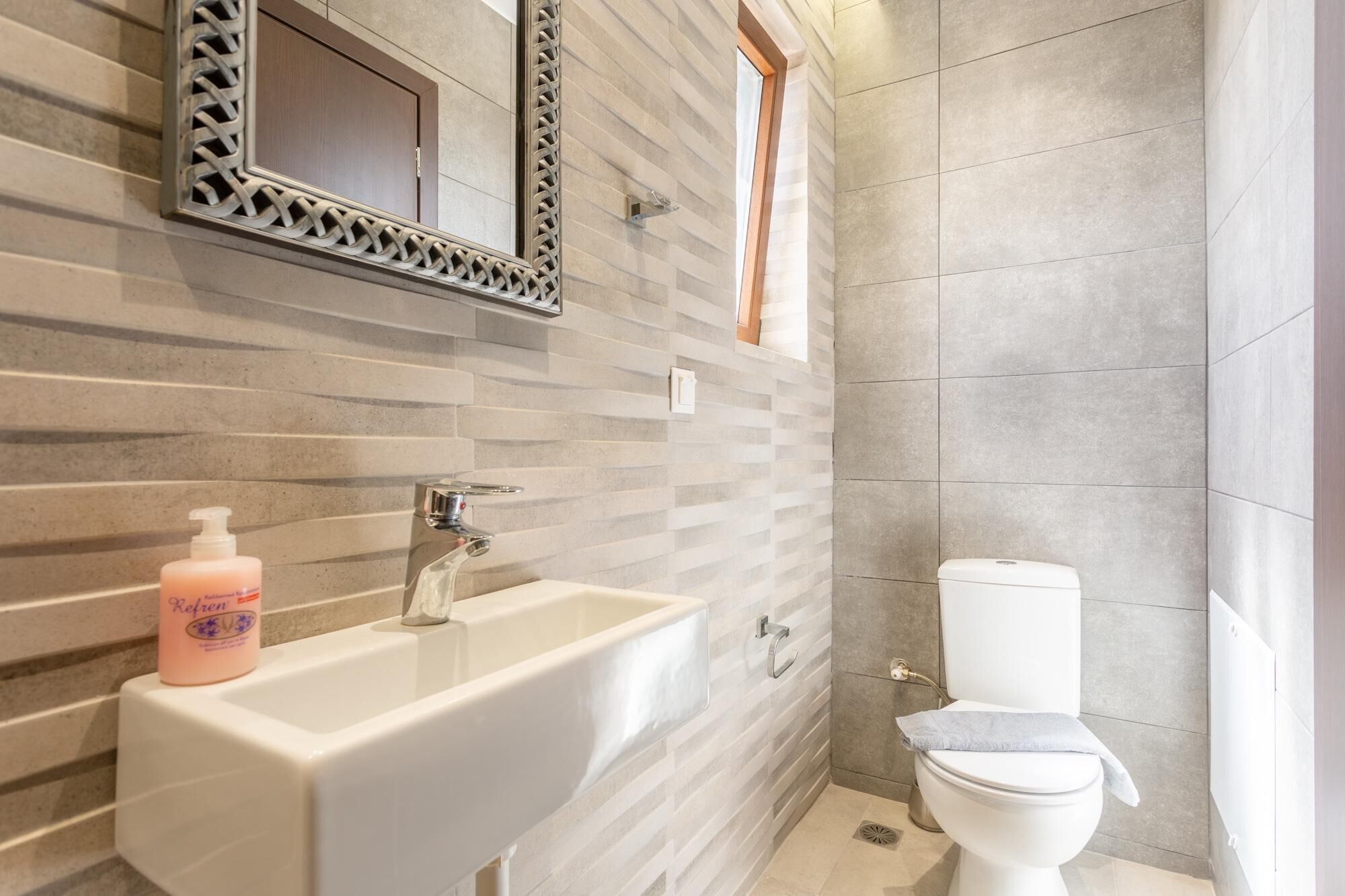 Een badkamer met een witte wastafel, een spiegel met decoratieve lijst, een toilet en een douchegedeelte.