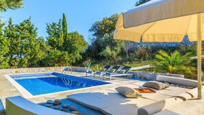 Zona de piscina con sillones reclinables, una sombrilla y un muro de piedra.
