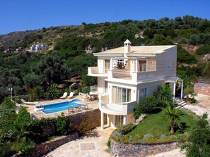 A multi-story villa with a swimming pool, outdoor seating, and a view of the surrounding hills.
