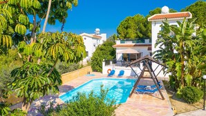 A pool area with a swing set, surrounded by lush greenery and a white building with a tiled roof. - Villa Charoula Tria Large Private Pool A C Wifi - 3273 (Polis)