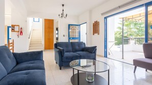 Amplio salón con un sofá azul, una mesa de centro de vidrio y vistas a un balcón con mobiliario exterior.