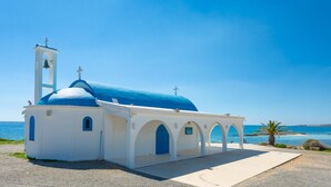 Una iglesia blanca con cúpula azul y un campanario frente al mar.