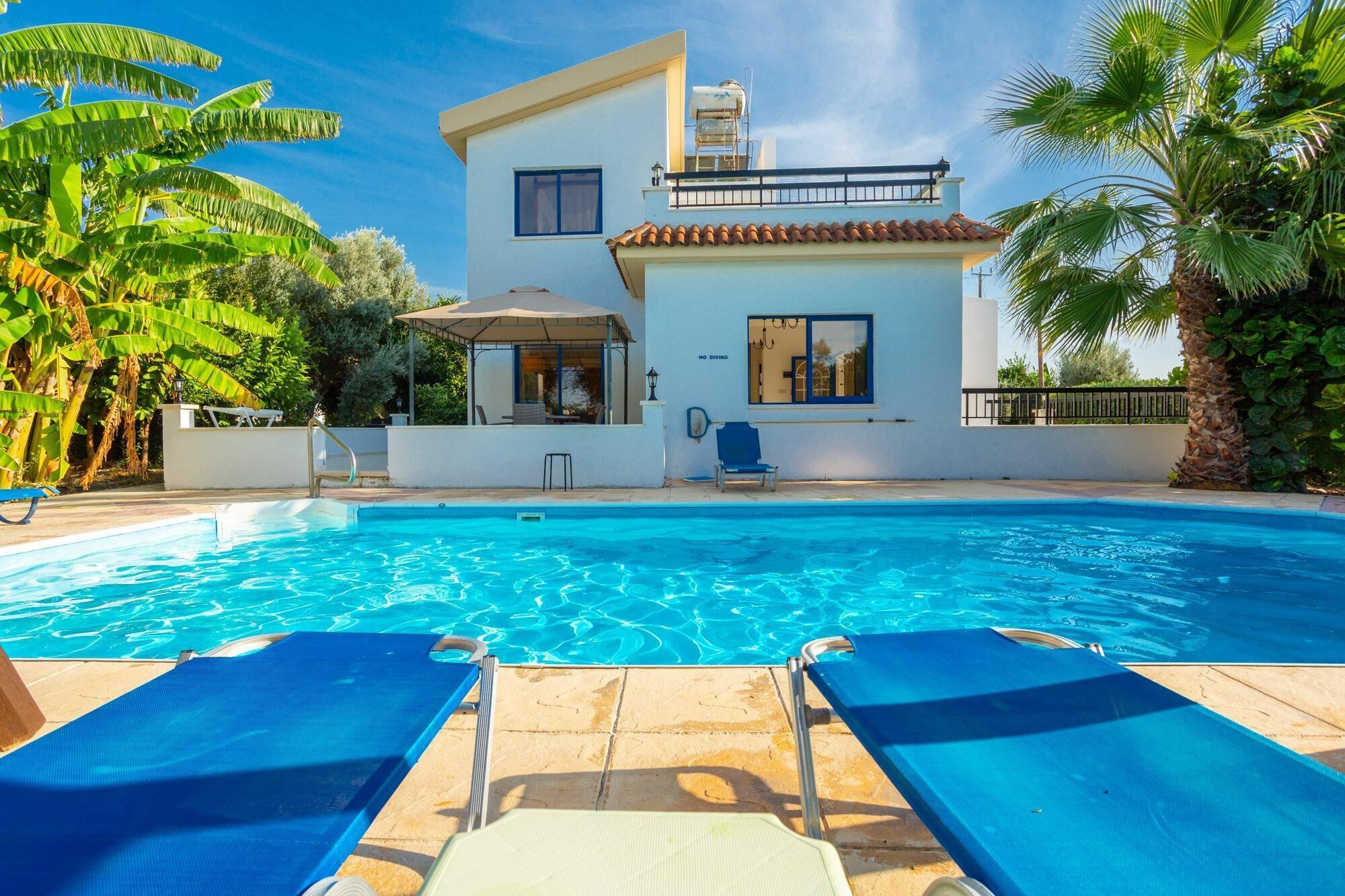 A swimming pool with lounge chairs, a covered patio, and a modern two-story building with a water tank on the roof.