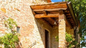 Un bâtiment en pierre avec un escalier en bois menant à une porte, le tout entouré de verdure et de fleurs.