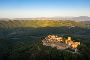 A historic stone building with multiple towers, surrounded by lush green hills and a clear sky.
